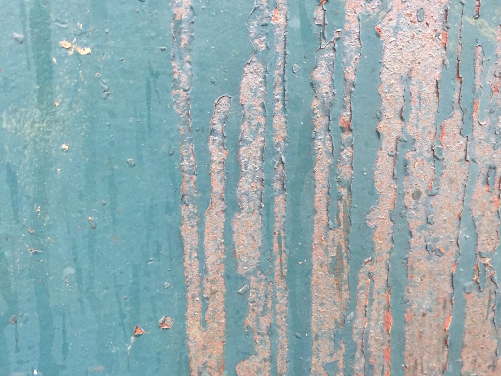 Dirty teal paint over very rusty metal with chips