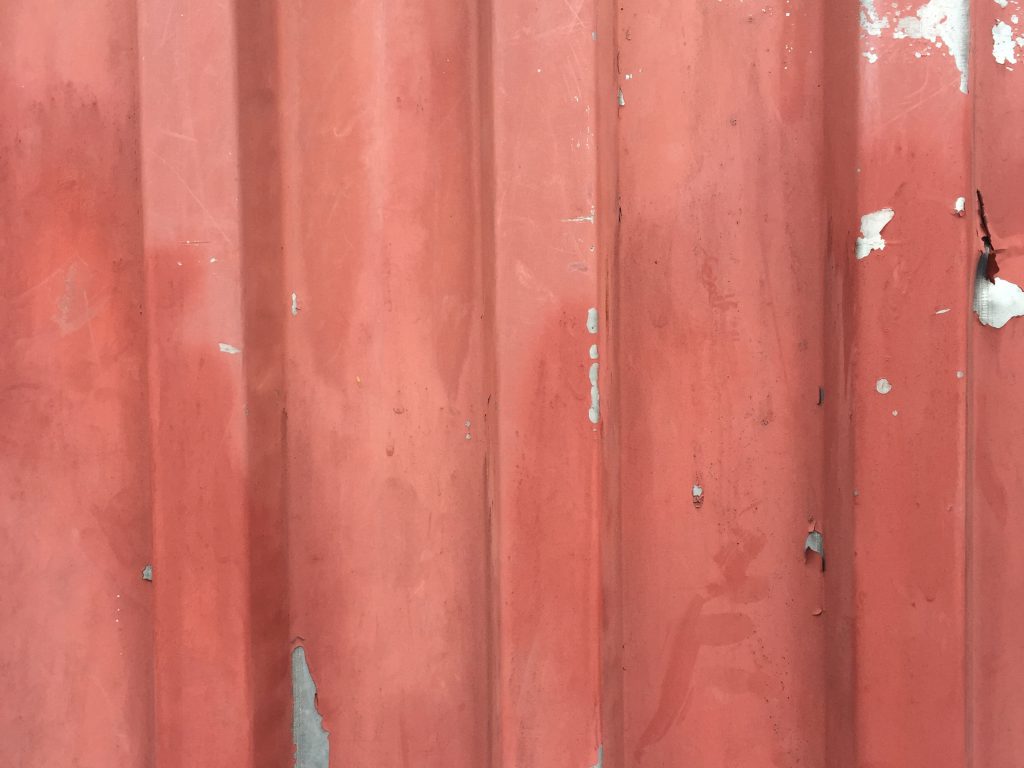 Faded red paint pealing back from metal wall