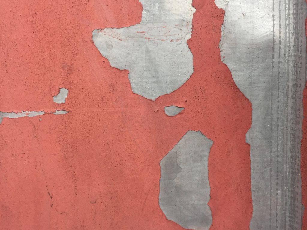 Red paint that is dirty and chipping over metal surface
