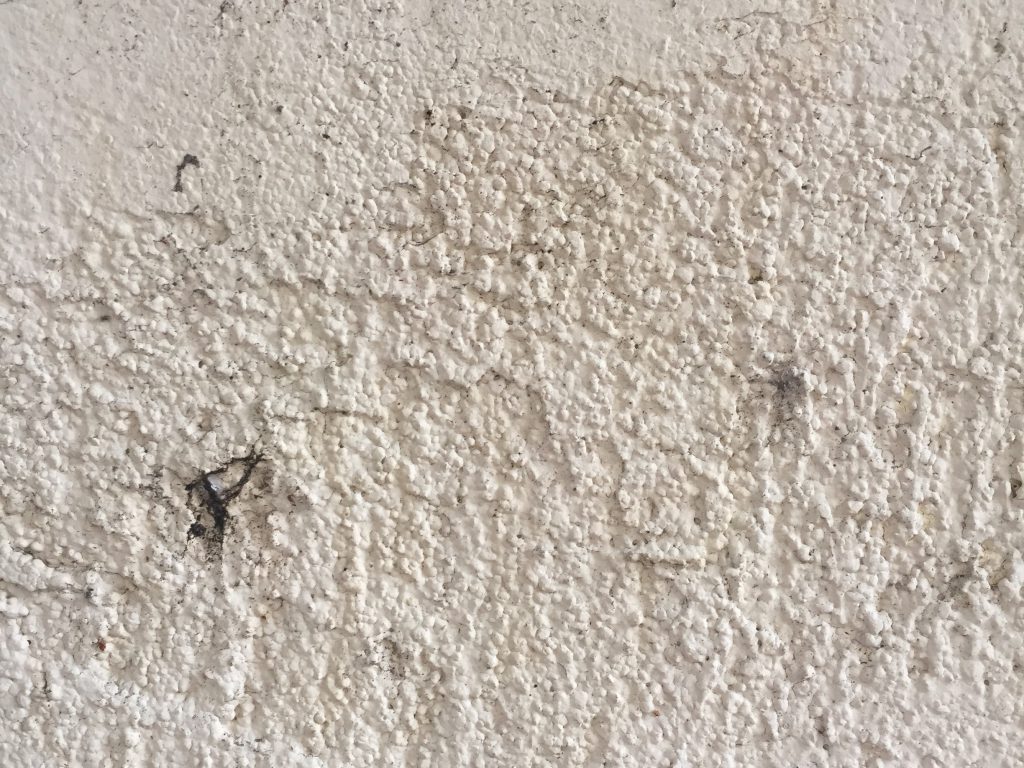White concrete stucco wall with patches and dirt