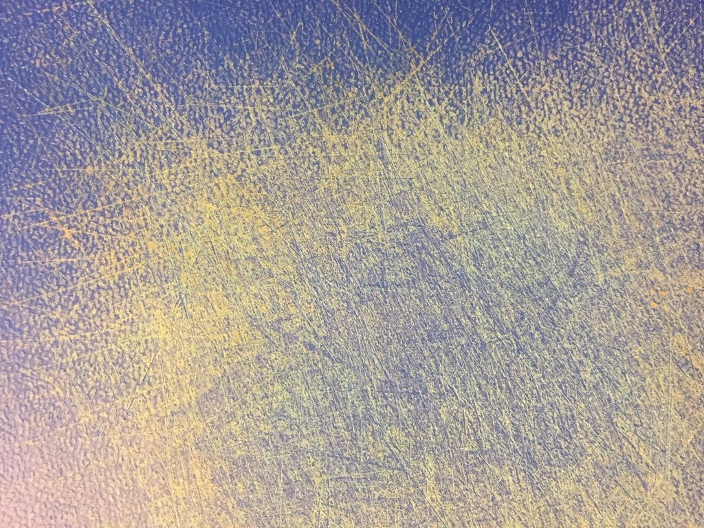 Yellow and blue plastic cutting board with tons of scratch marks