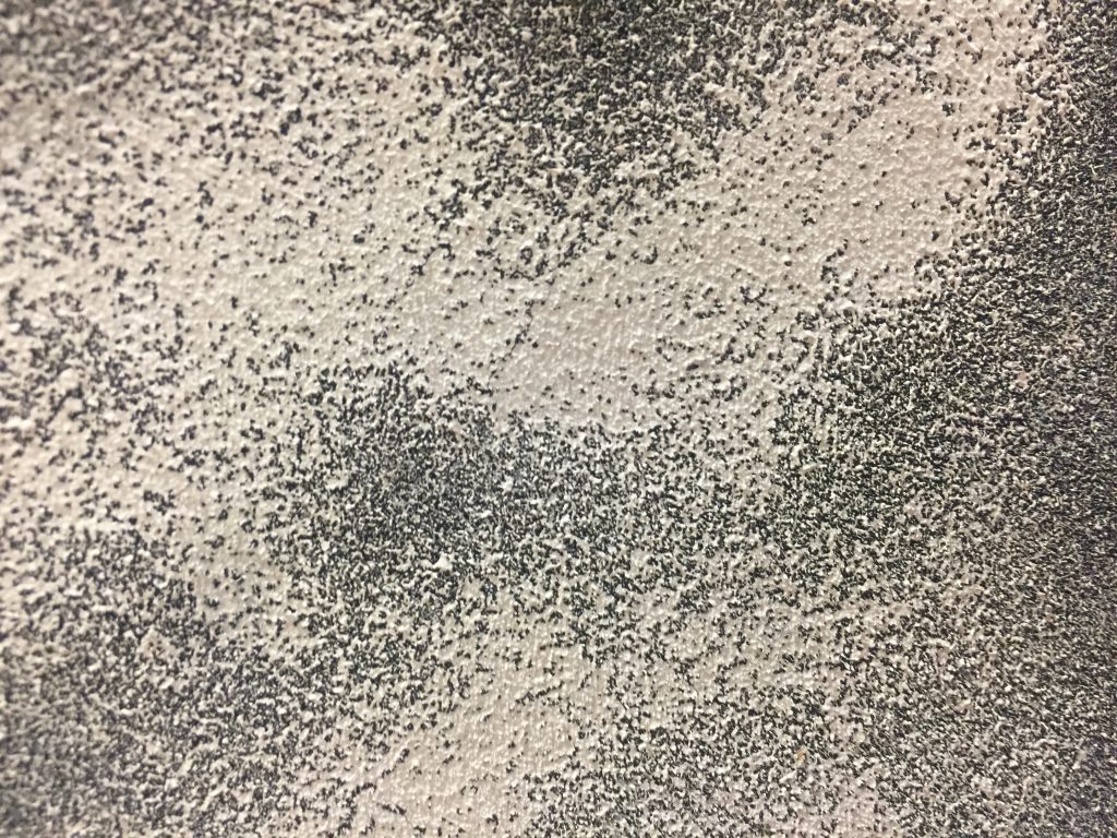 Off white layer of paint over dark grey textured surface