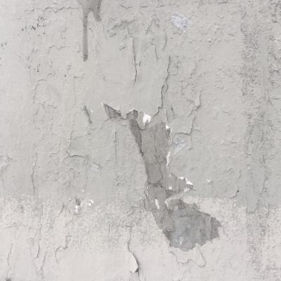 Cracked and dirty concrete wall with chipping white paint