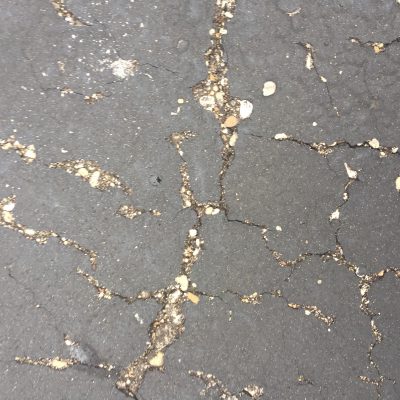 Cracked blacktop with gravel and concrete in between