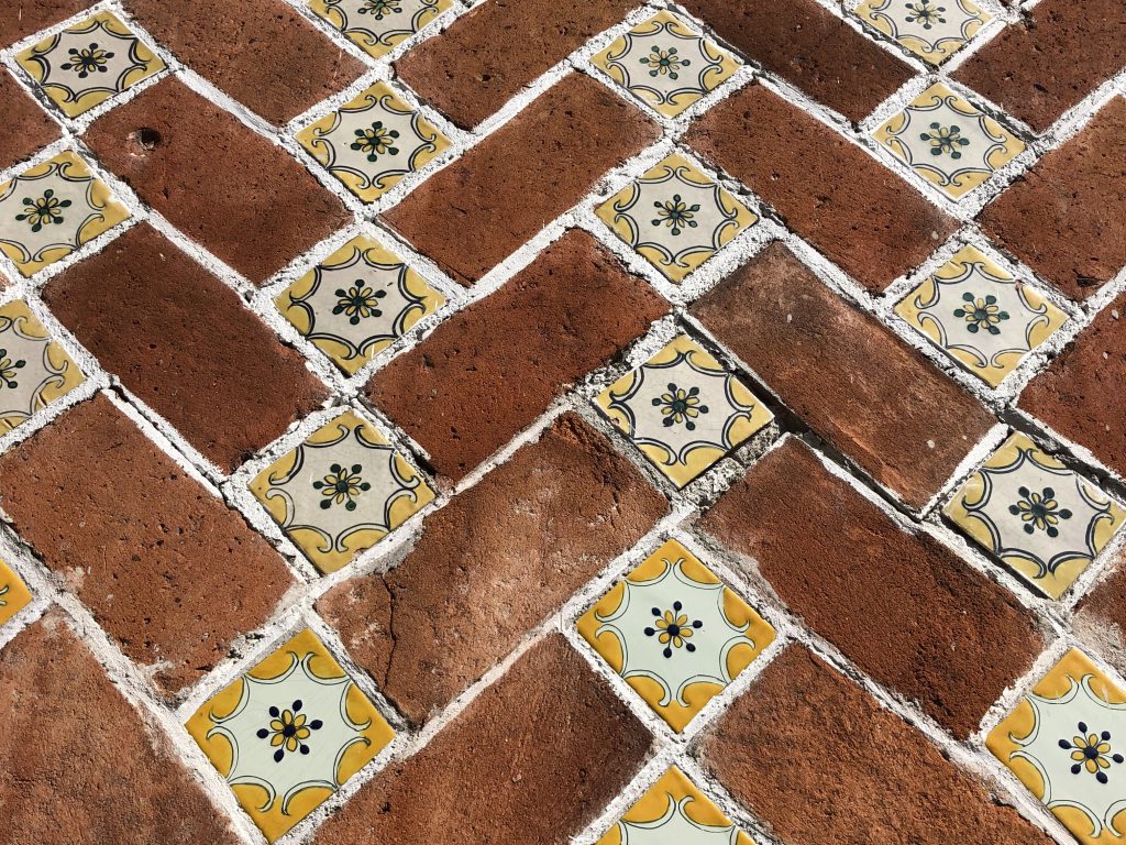 Textured bricks and square titles with ornate yellow flower in middle organized in a pattern.