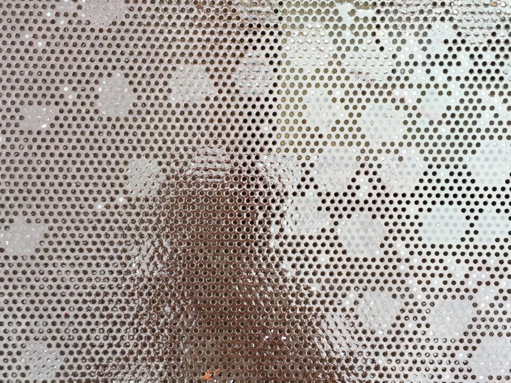 Metal grate with small holes that is wet and shiny texture