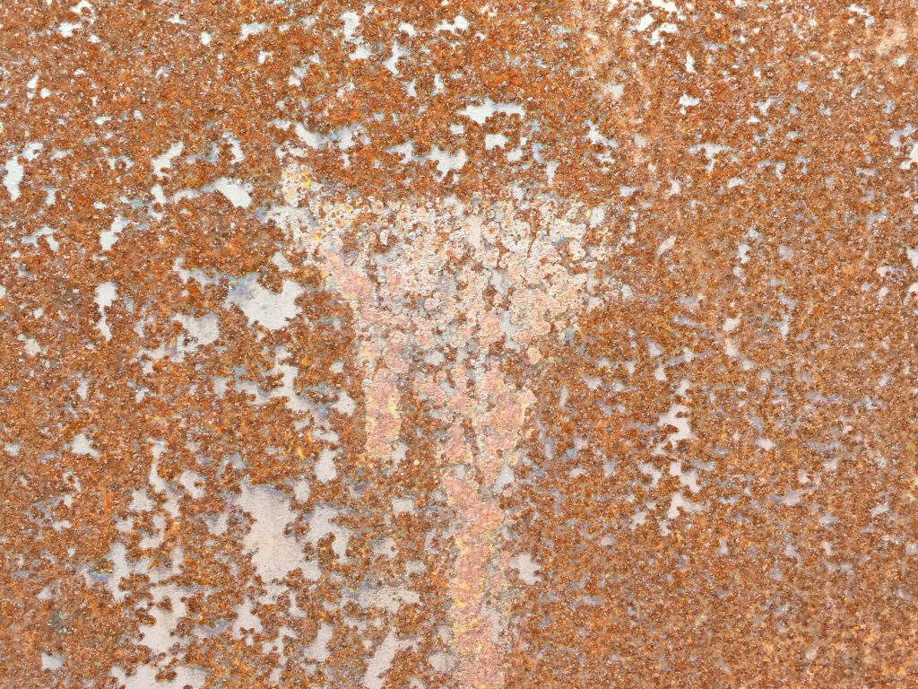 Close up of deep red rust on metal surface with lots of flakes and texture