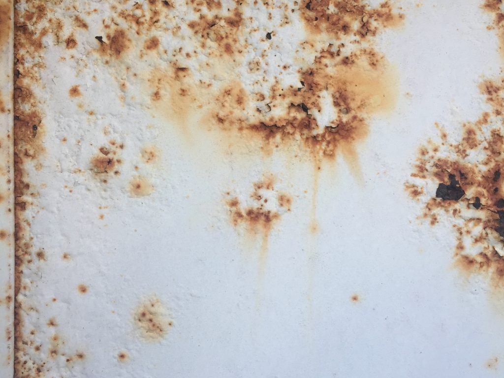 Bright white paint stained with red-brown rust seeping through layers of paint