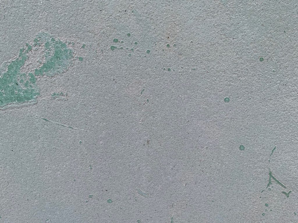 Concrete wall with coarse surface and sparse chips of teal paint