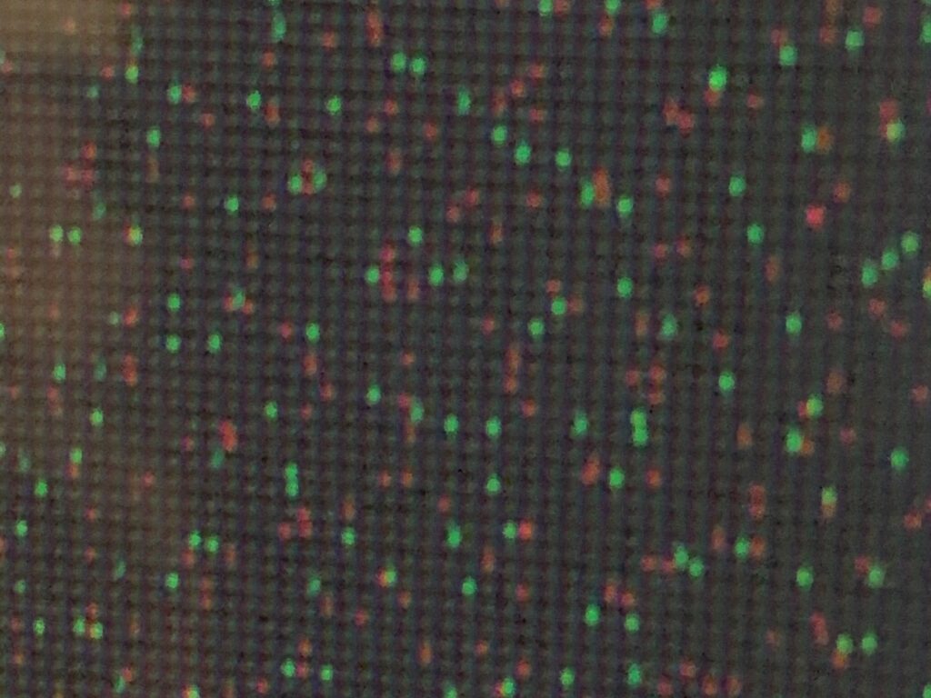 Blurry pixel close up of tv screen featuring red and green dots on black