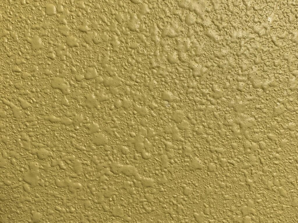 Pale yellow paint over textured stucco wall