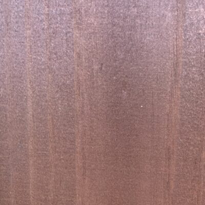 Extreme close up of wood board with redish hue, visible grain and very slight cracks.